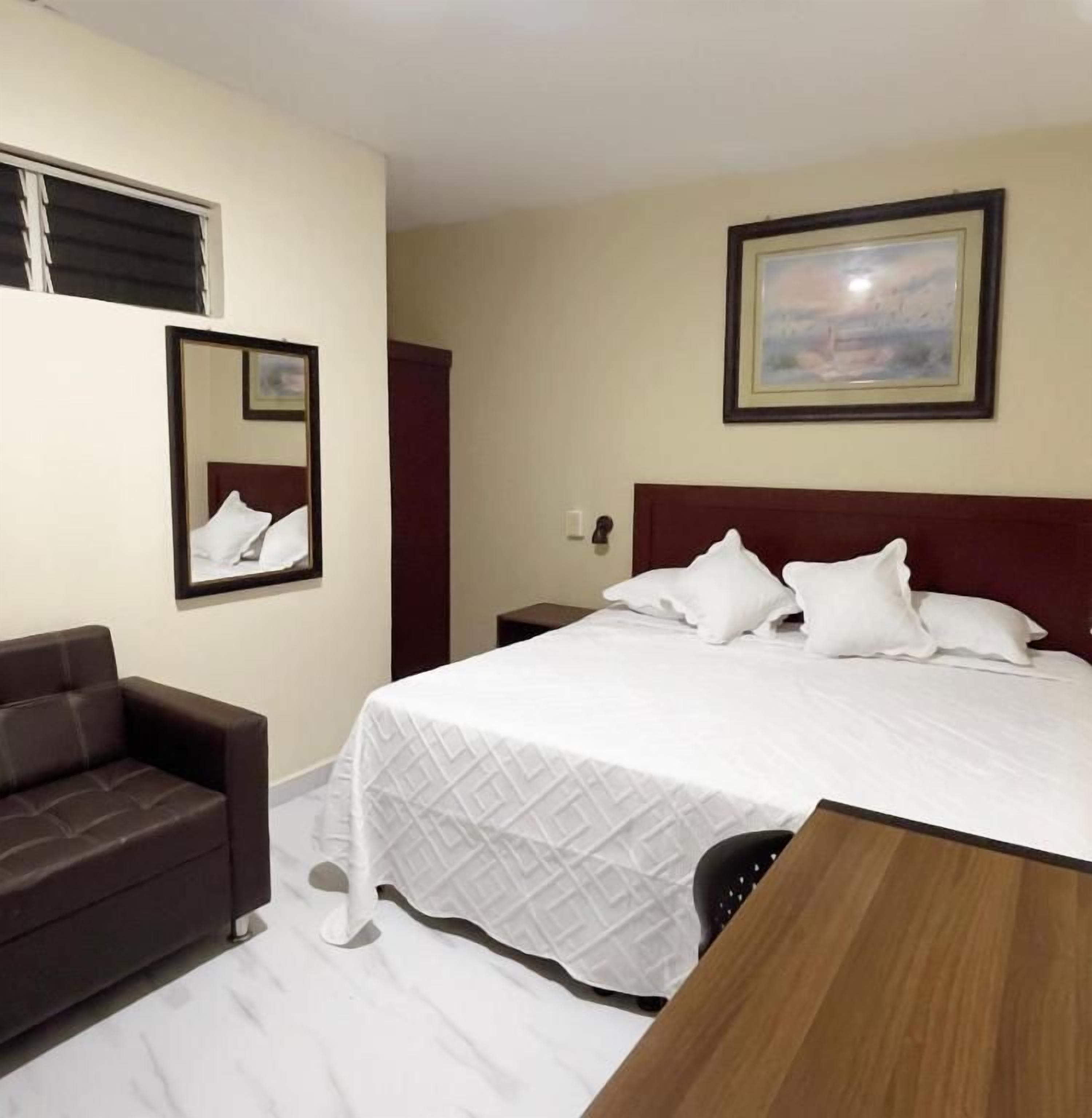 Une chambre d’hôtel avec un lit, un canapé, une table en bois, un miroir et un tableau accroché au mur.