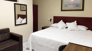 Quarto de hotel com uma cama, um sofá, uma mesa de madeira, um espelho e um quadro na parede.