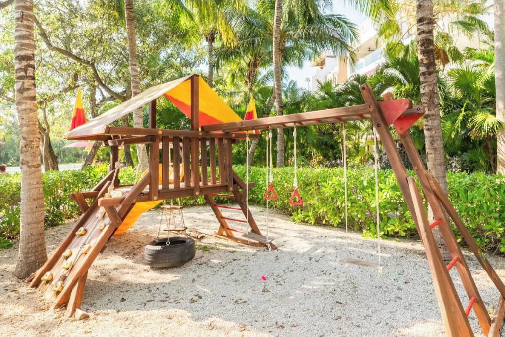 A wooden swing set with a tire swing, surrounded by palm trees and greenery.