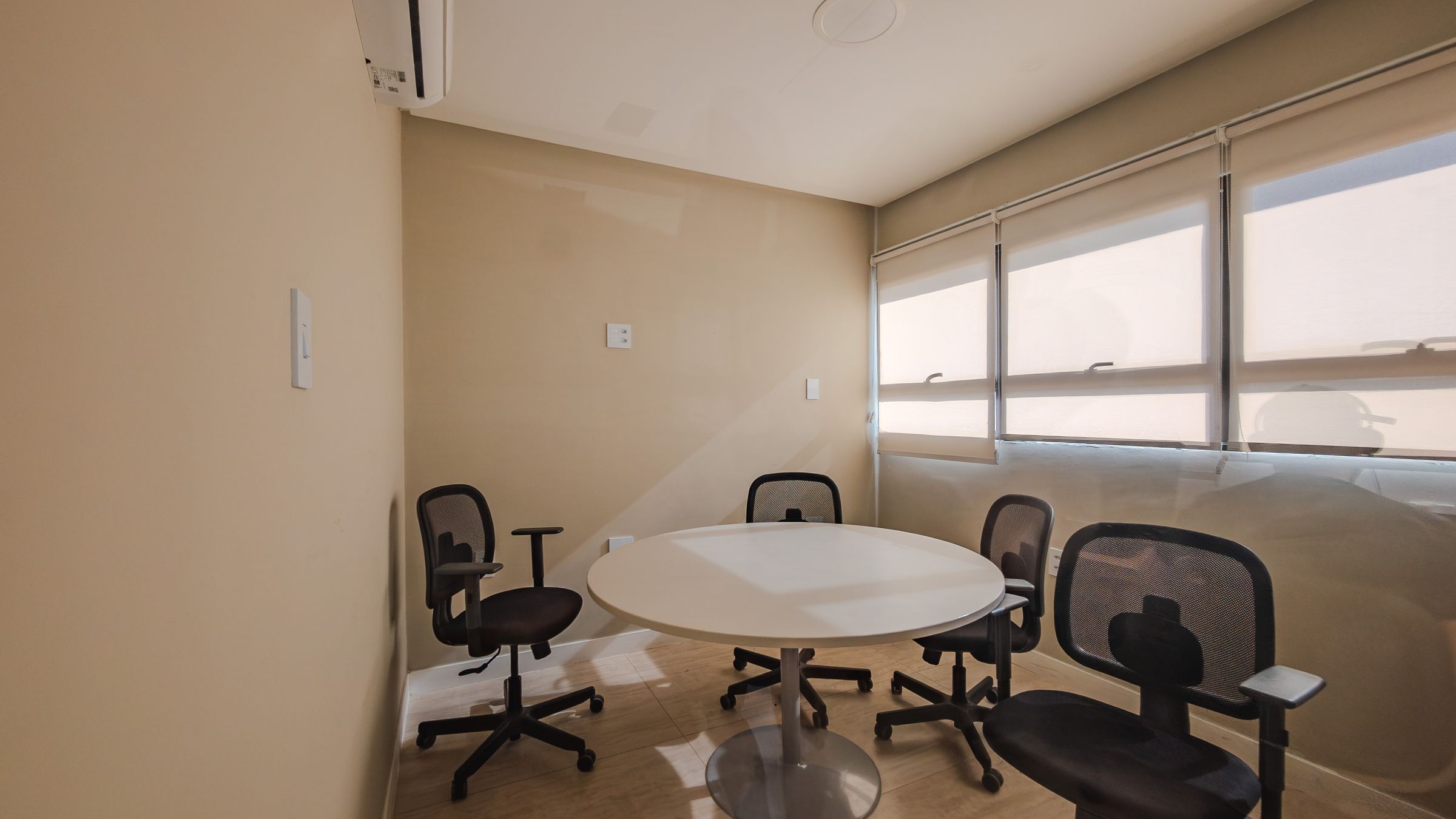 Une salle de conférence équipée d’une table ronde, de quatre chaises de bureau et d’une grande fenêtre avec des stores.