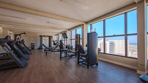 Een fitnessruimte met loopbanden, krachttrainingsapparatuur en uitzicht op de stad door grote ramen.