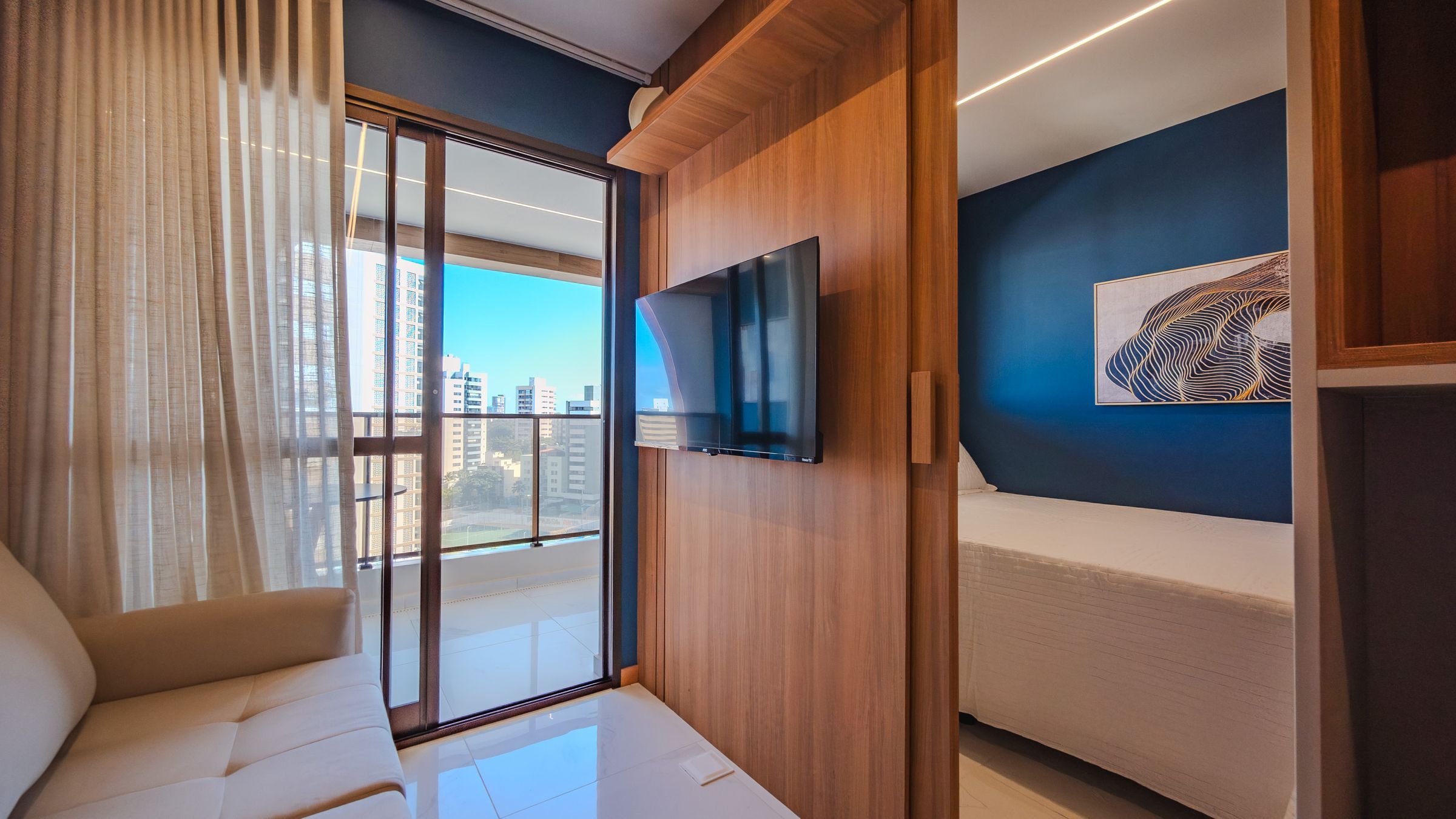 Ein modernes Schlafzimmer mit einer Glasgleittür, die auf einen Balkon führt, einem an der Wand montierten Flachbildfernseher und einem abstrakten Kunstwerk.