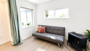 Ein modernes Wohnzimmer mit einem grauen Sofa, zwei Fenstern, einem schwarzen Heizgerät und einem grünen Vorhang.