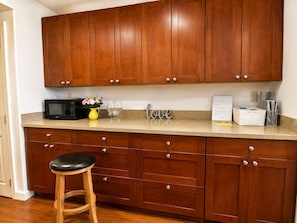 A kitchen with wooden cabinets, a microwave, a vase with flowers, and a stool.