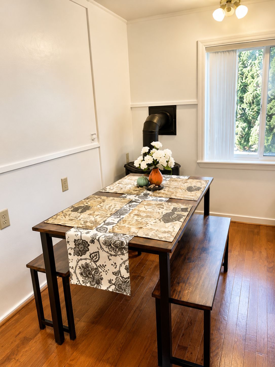 A dining table with a patterned table runner, a vase with white flowers, and a bench.