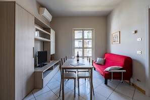 Un espacio habitable compacto con zona de comedor, un sofá rojo y un televisor.