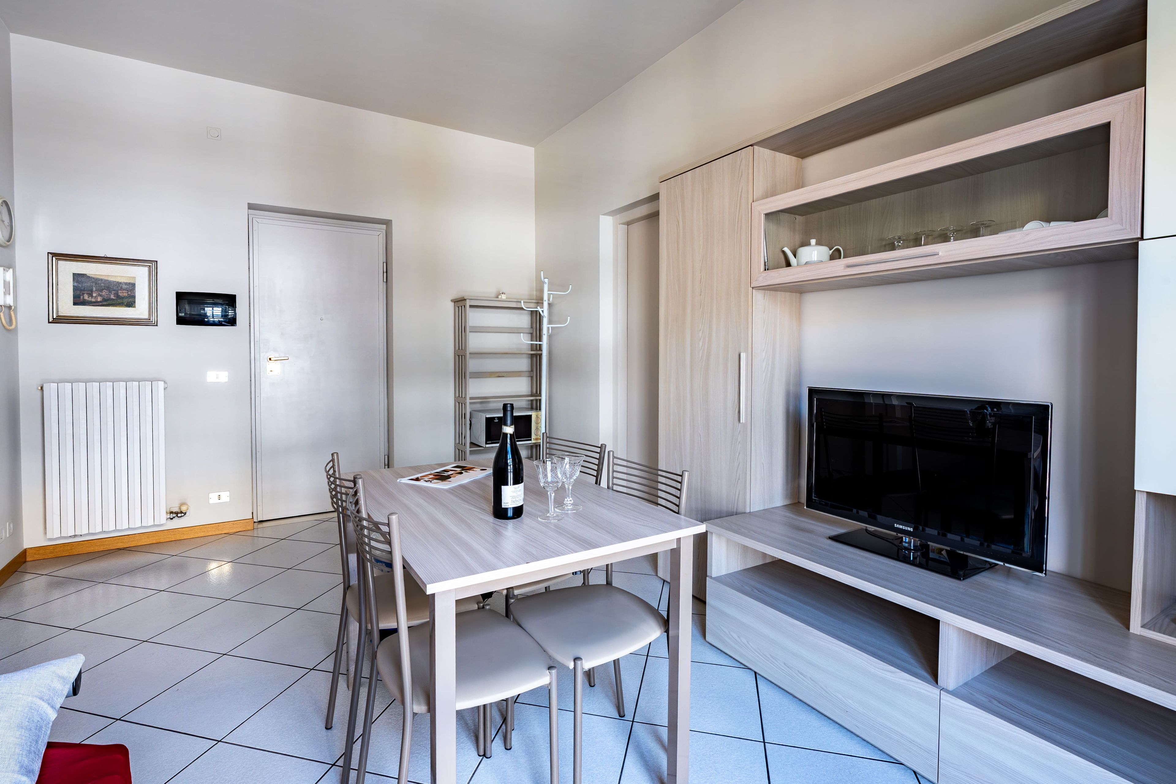 Un coin repas moderne avec une table, des chaises, une bouteille de vin et des verres. Un téléviseur est posé sur un meuble à droite.