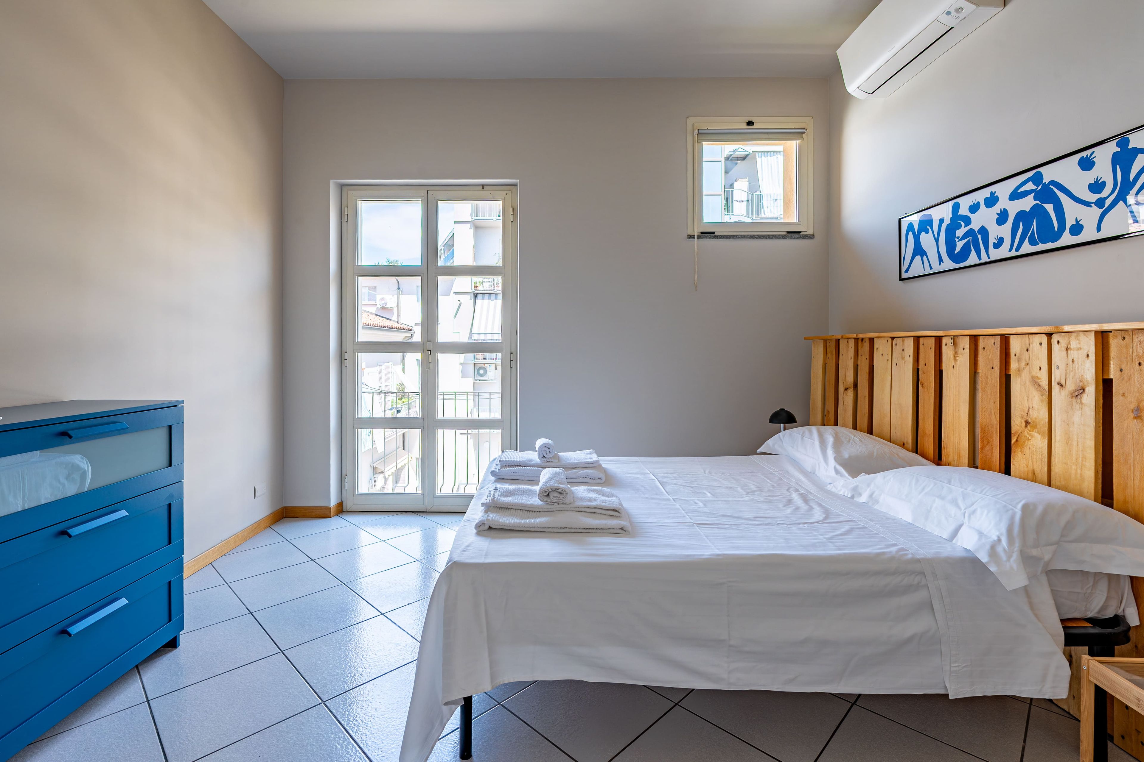 Une chambre à coucher avec un lit, une commode bleue, une fenêtre et un climatiseur fixé au mur.