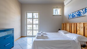 Un dormitorio con una cama, un aparador azul, un ventanal y un aire acondicionado instalado en la pared.
