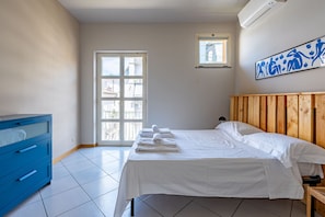 Een slaapkamer met een bed, een blauwe ladekast, een raam en een wandairconditioner.