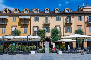 A building with multiple balconies, outdoor seating with umbrellas, and a clear sky. - Casa Savona nel cuore di Alba (Alba)