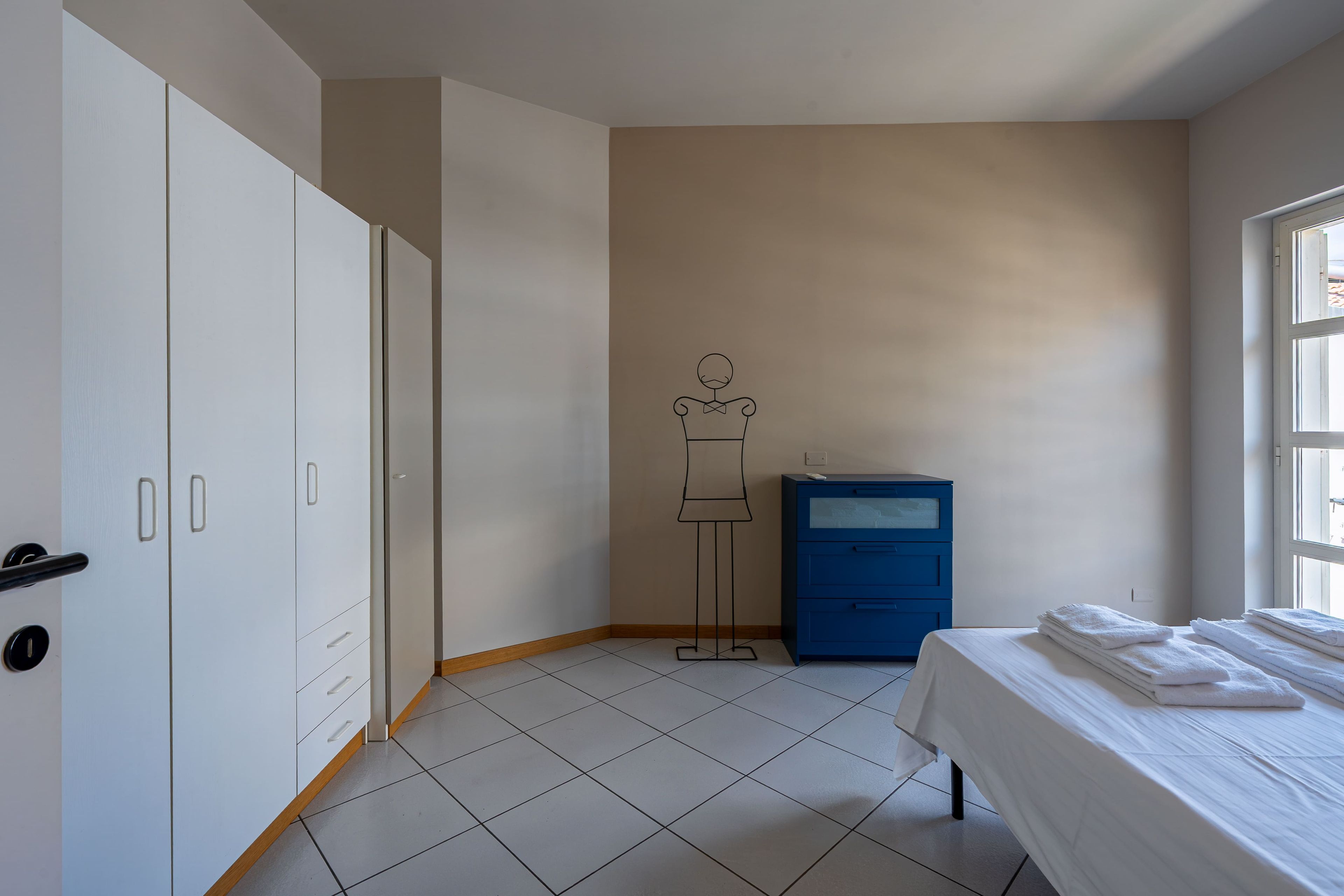 A bedroom with a bed, a wardrobe, a desk, and a window.