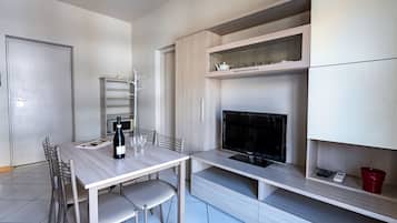 A modern kitchen with a dining table, chairs, a wine bottle, and a television.