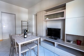 Una cocina moderna con una mesa de comedor, sillas, una botella de vino y un televisor.