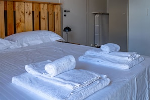 A neatly made bed with white linens and rolled towels, a wooden headboard, a bedside lamp, and a radiator. - Casa Savona nel cuore di Alba (Alba)