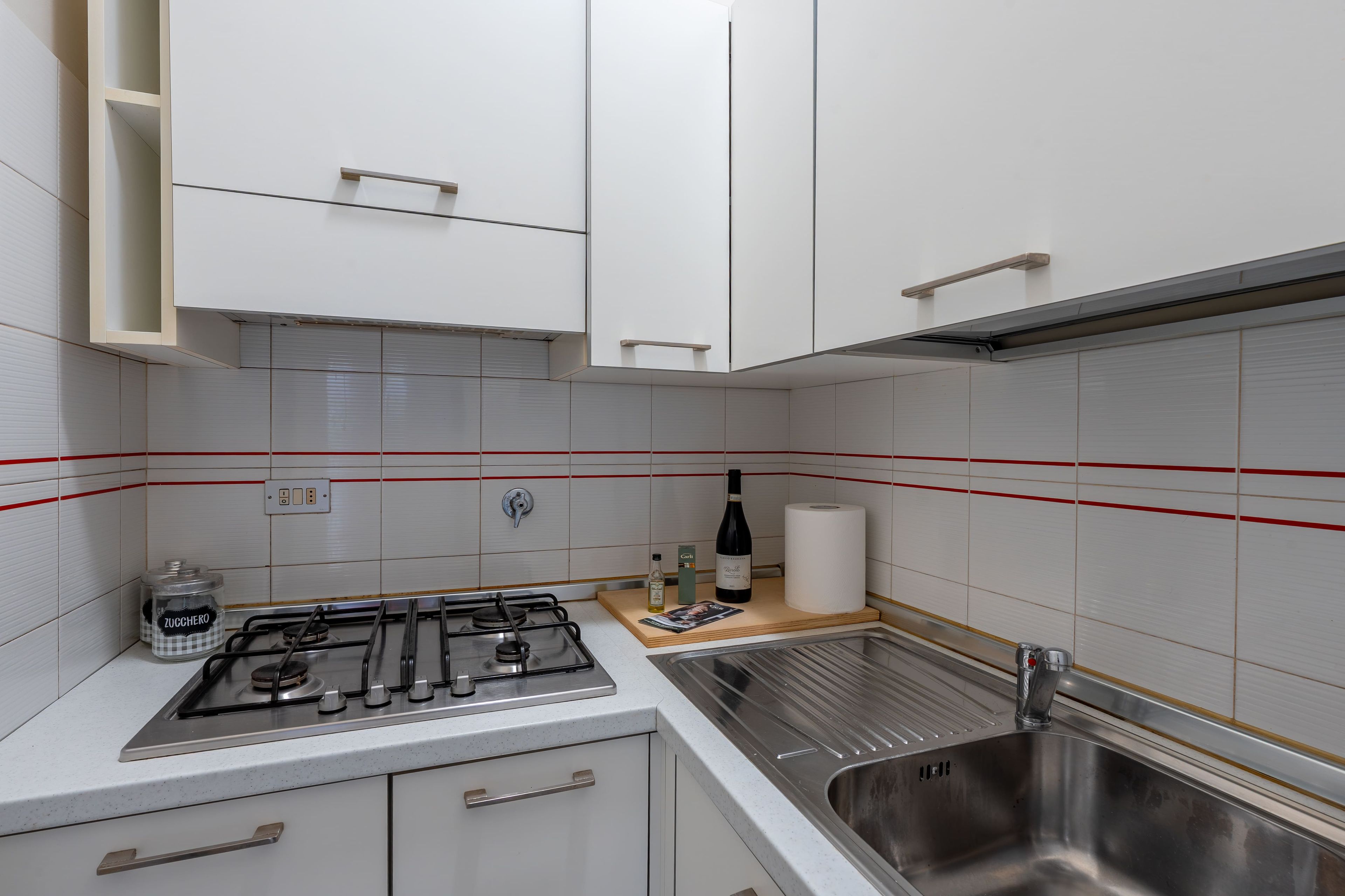 A kitchen with white cabinets, a stainless steel sink, a gas stove, and a red-striped backsplash.