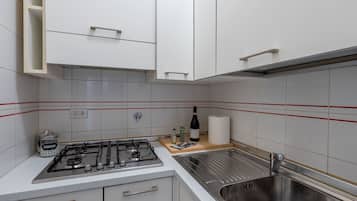 A kitchen with white cabinets, a stainless steel sink, a gas stove, and a red-striped backsplash.