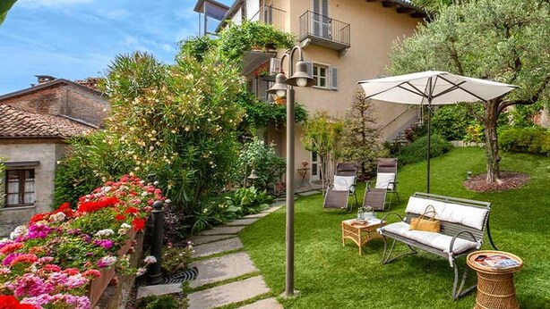 En bostadsfastighet med en välskött trädgård, utomhusmöbler och ett tvåvåningshus med balkonger.