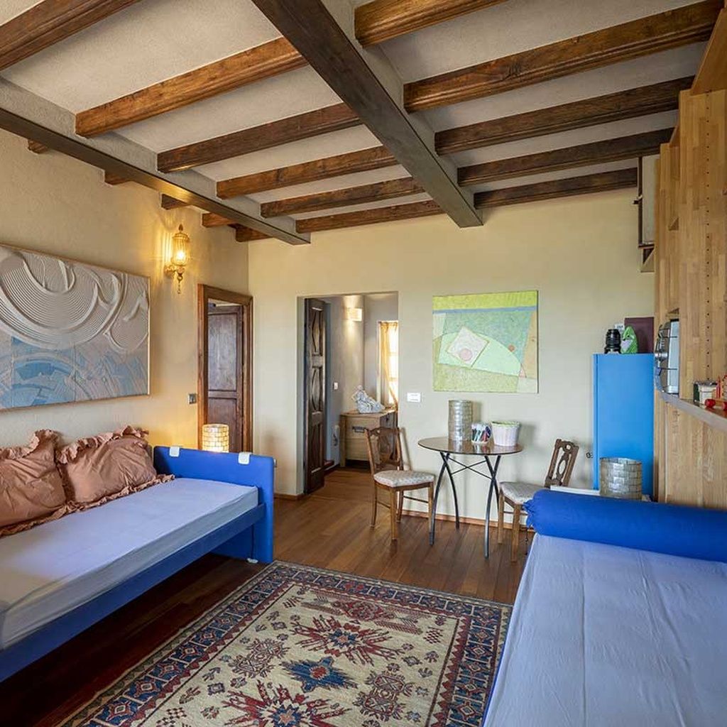 Une pièce confortable avec un lit, un canapé, une petite table et des chaises. Le plafond est en bois et les poutres sont apparentes.