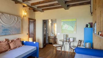 Une pièce confortable avec un lit, un canapé, une petite table et des chaises. Le plafond est en bois et les poutres sont apparentes.