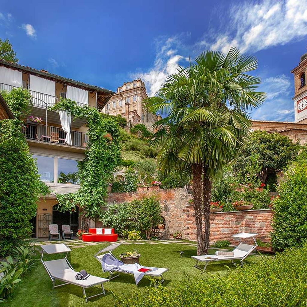 Une cour avec des fauteuils de jardin, un palmier et un bâtiment historique doté d’un clocher.