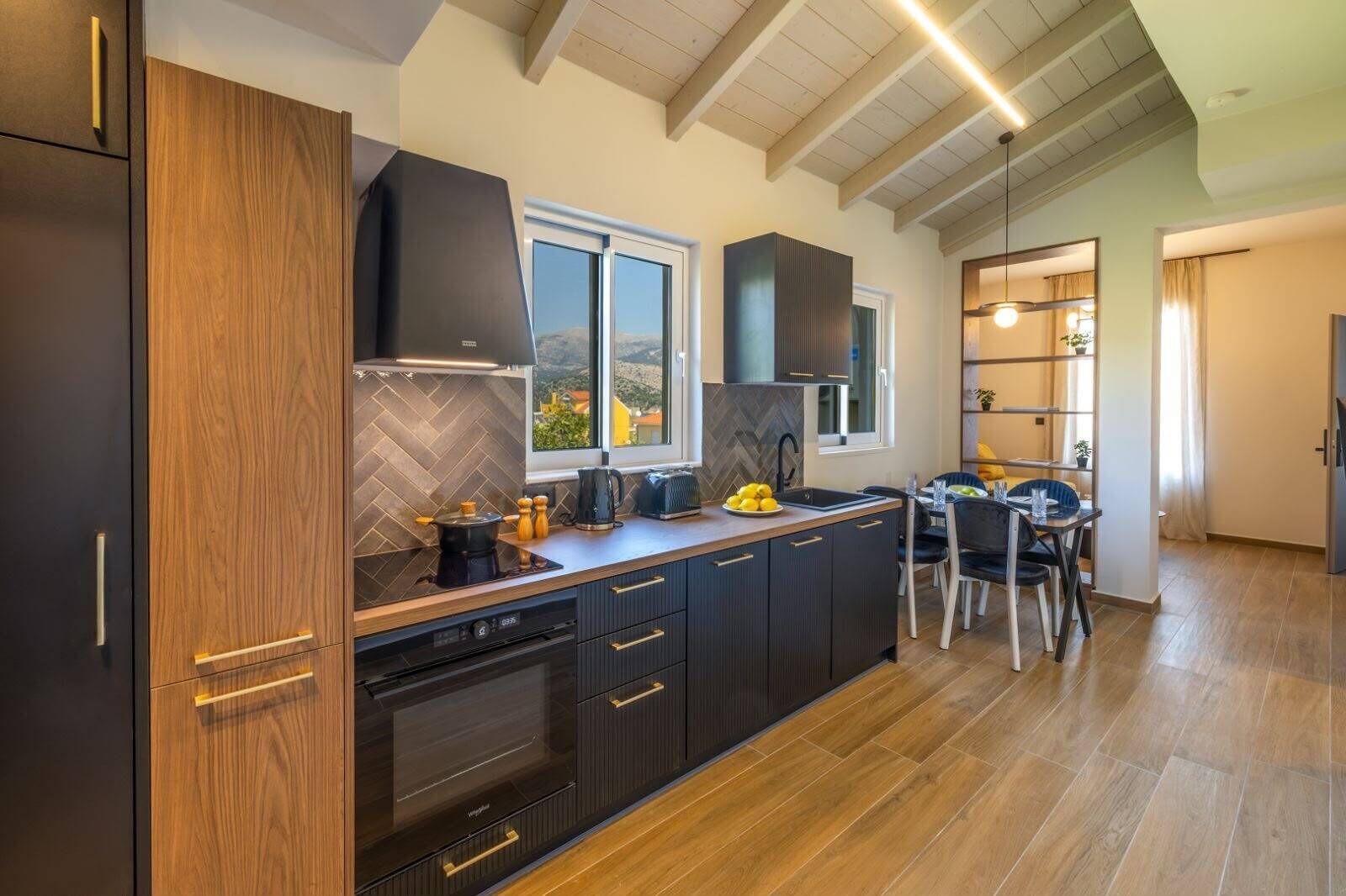 A modern kitchen with a large island, dark cabinetry, and a view of the outdoors.