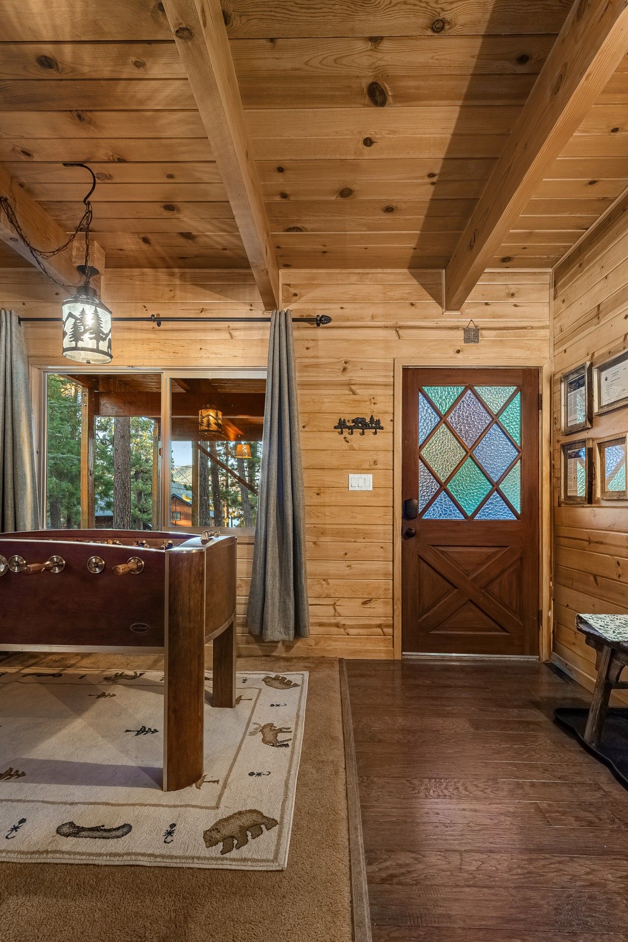 A wooden interior with a pool table, a door with a stained glass window, and a view through a window.