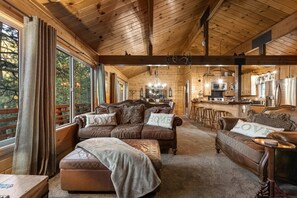 A cozy log cabin interior with a living room, a kitchen, and a bar area. - Heavenly Bay Retreat | Hot Tub, Lake View & Games! (Big Bear Lake)