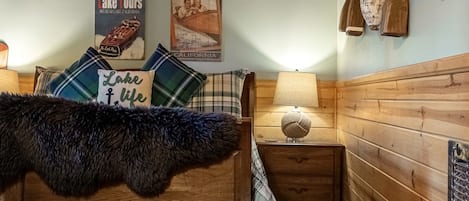 Un dormitorio estilo cabaña acogedor, con una cama de madera, una mesita de noche, una lámpara y un estante montado en la pared con objetos decorativos.
