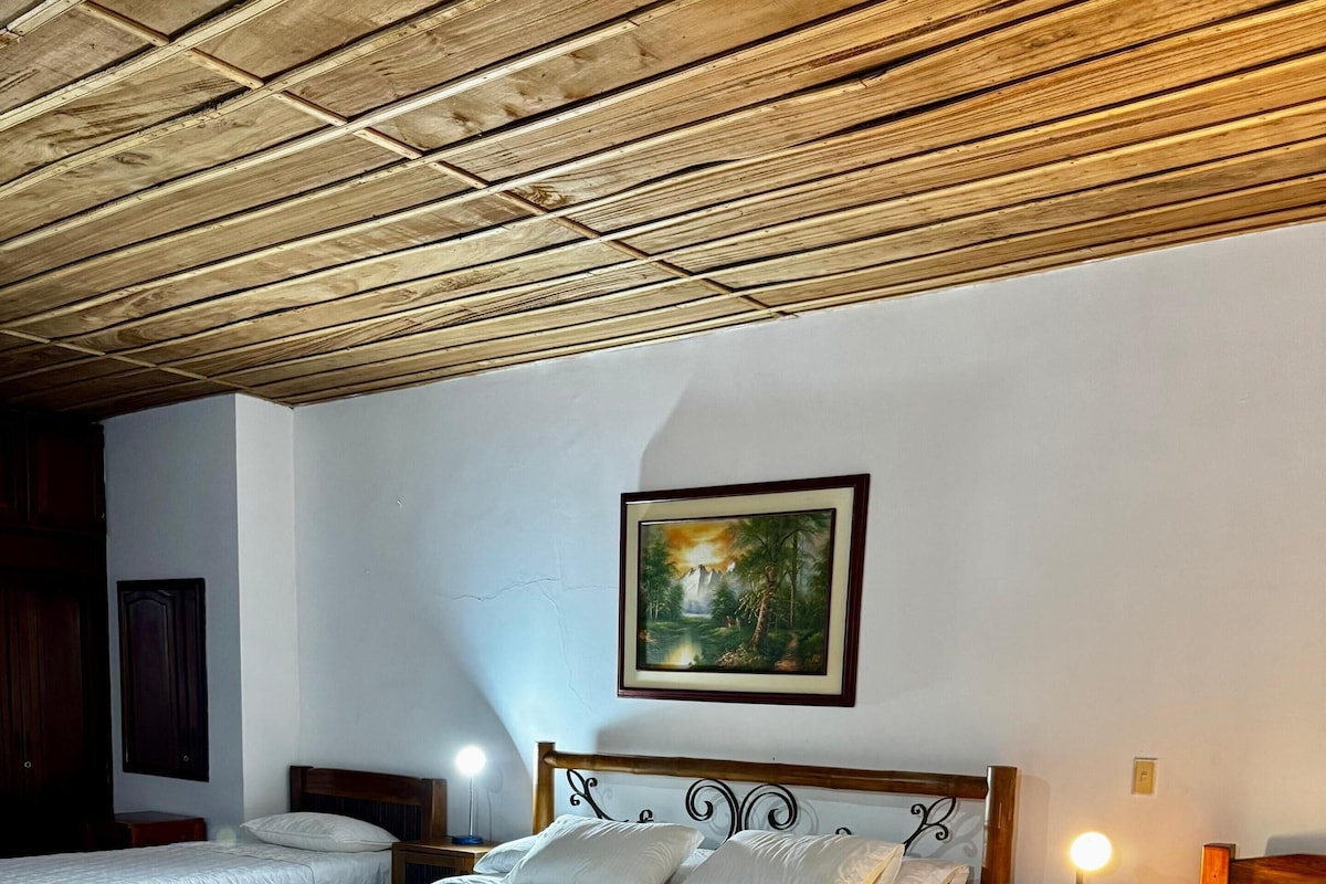 Ein Schlafzimmer mit zwei Betten, einer Holzbalkendecke, einem Bild an der Wand und einem Nachttisch mit einer Lampe.