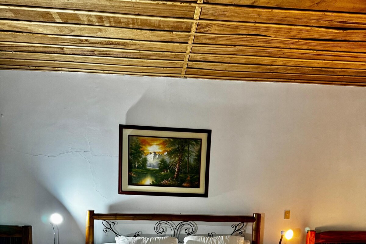 Ein Schlafzimmer mit einem hölzernen Bett, weißer Bettwäsche, einem gerahmten Landschaftsbild und zwei Nachttischlampen.