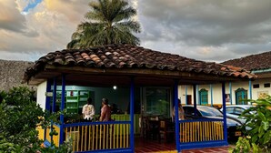 A building with a tiled roof, a covered porch, and a palm tree in the background. - Aramat La Joya (Calarcá)