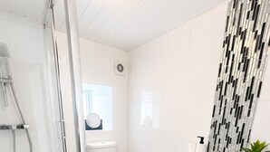 A modern bathroom with a glass shower enclosure, a toilet, a sink with a mirror, and a decorative wall panel. - 4-Bed | New Cross to Central London in 20 Mins (London)