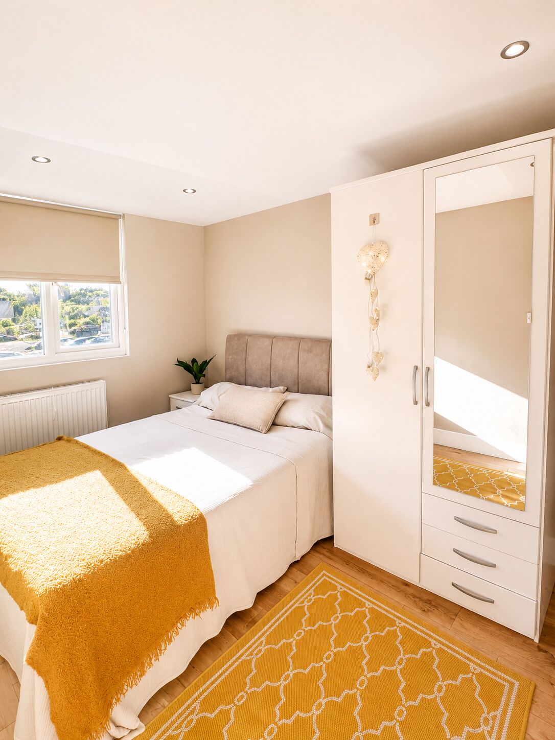 A bedroom with a bed, a wardrobe, a radiator, and a window.