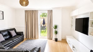 A modern living room with a sectional sofa, a flat-screen TV, and a large window with curtains. - 4-Bed | New Cross to Central London in 20 Mins (London)