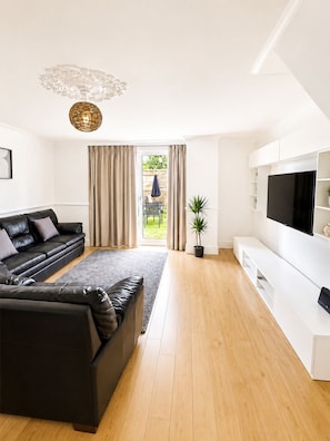 A modern living room with a sectional sofa, a flat-screen TV, and a large window with curtains. - 4-Bed | New Cross to Central London in 20 Mins (London)