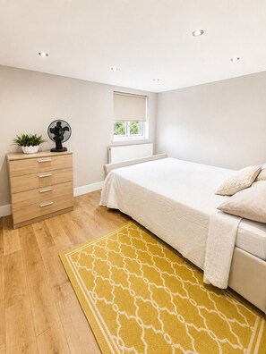 A bedroom with a bed, a dresser, a radiator, a window, and a fan. - 4-Bed | New Cross to Central London in 20 Mins (London)
