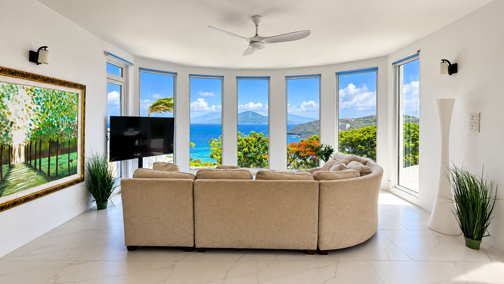 A modern living room with a curved sofa, a flat-screen TV, and large windows offering ocean views.