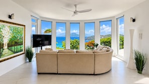 A modern living room with a curved sofa, a flat-screen TV, and large windows offering ocean views.