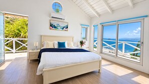 Une chambre à coucher avec un lit, une table de chevet, une fenêtre donnant sur la mer et un tableau accroché au mur.