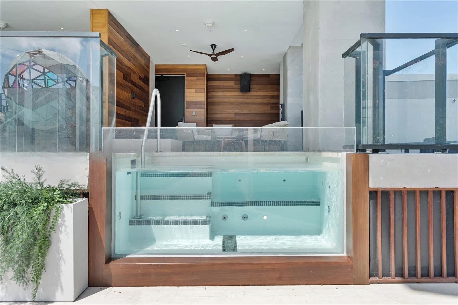 Un bain à remous extérieur moderne, doté d’une terrasse en bois, d’une enceinte en verre et d’un ventilateur de plafond.