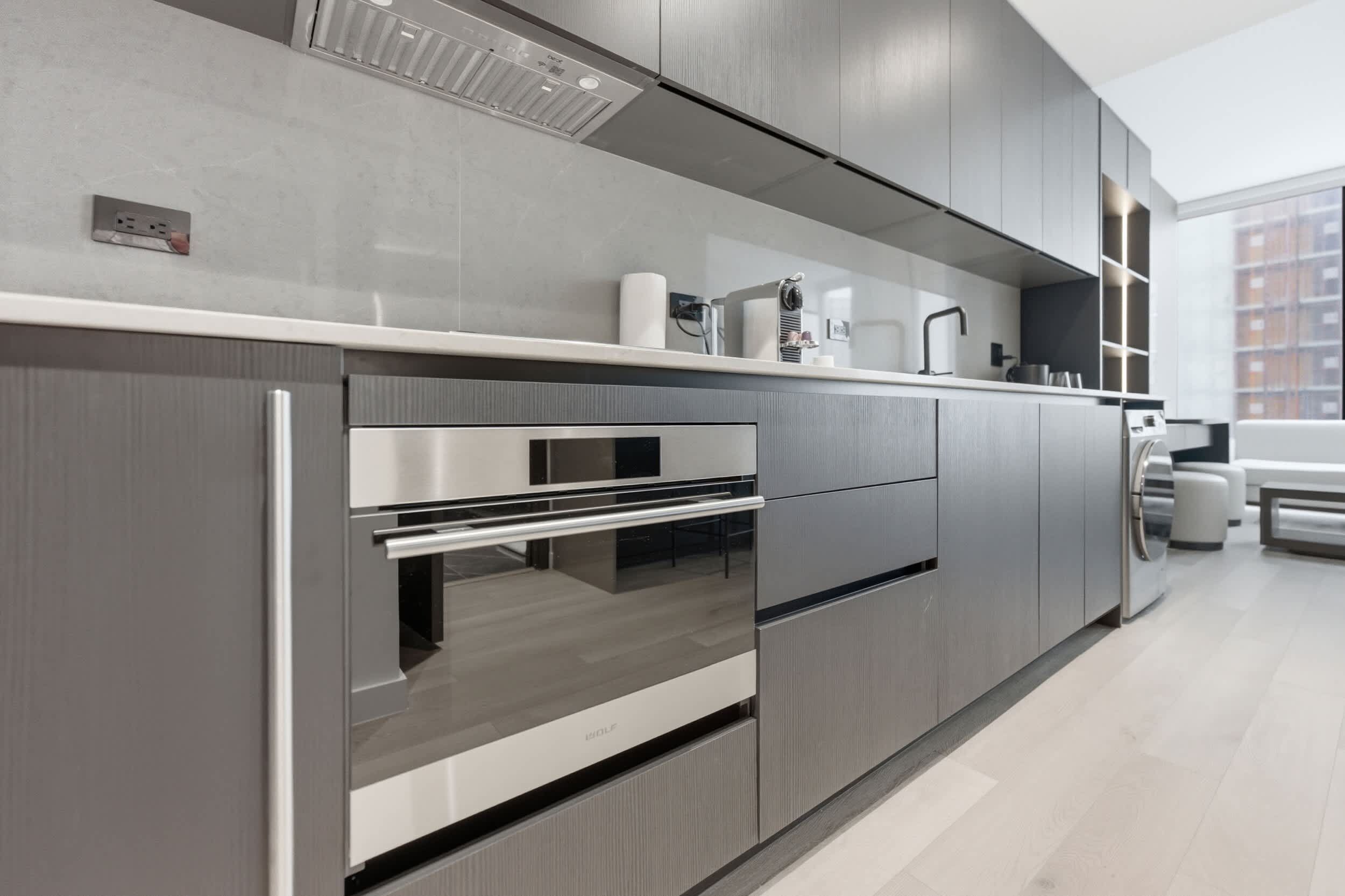 A modern kitchen with stainless steel appliances, grey cabinetry, and a built-in oven.