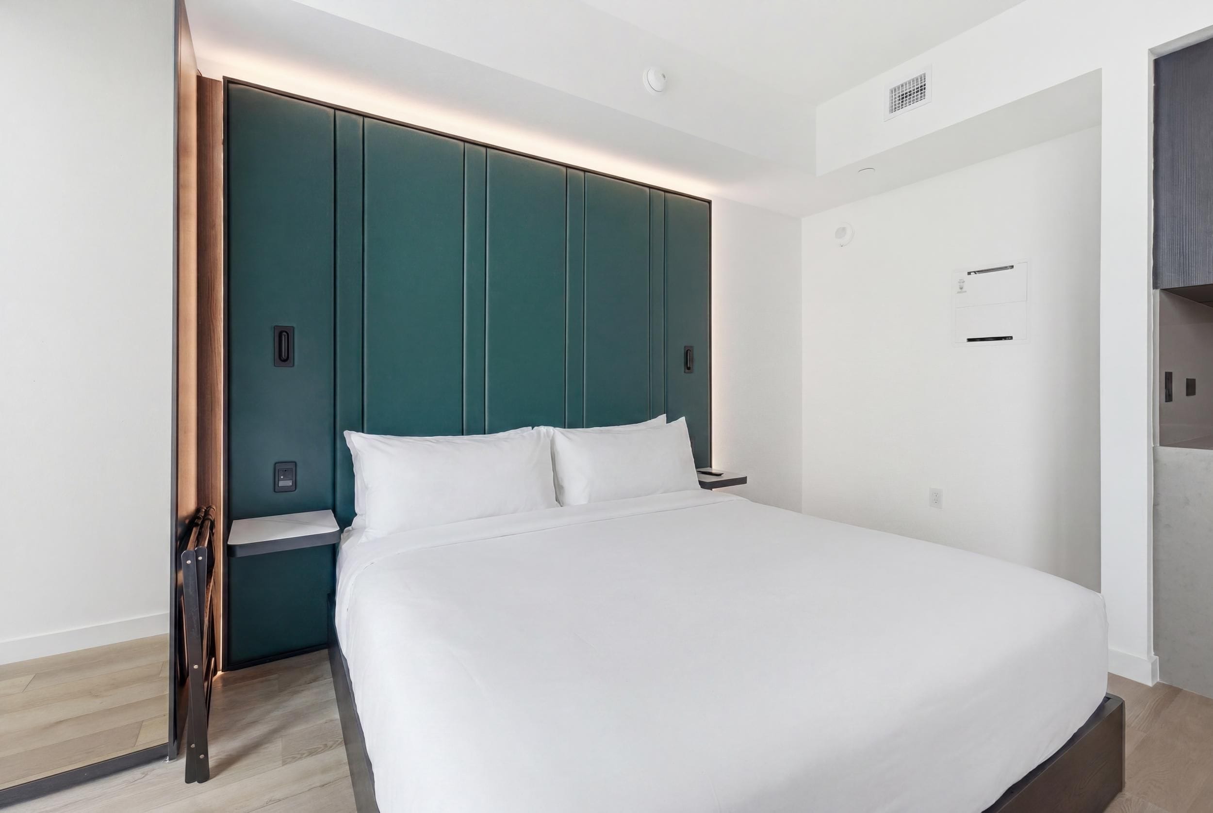 Et moderne hotelværelse med en stor seng, en væg i teal farve og trægulv.