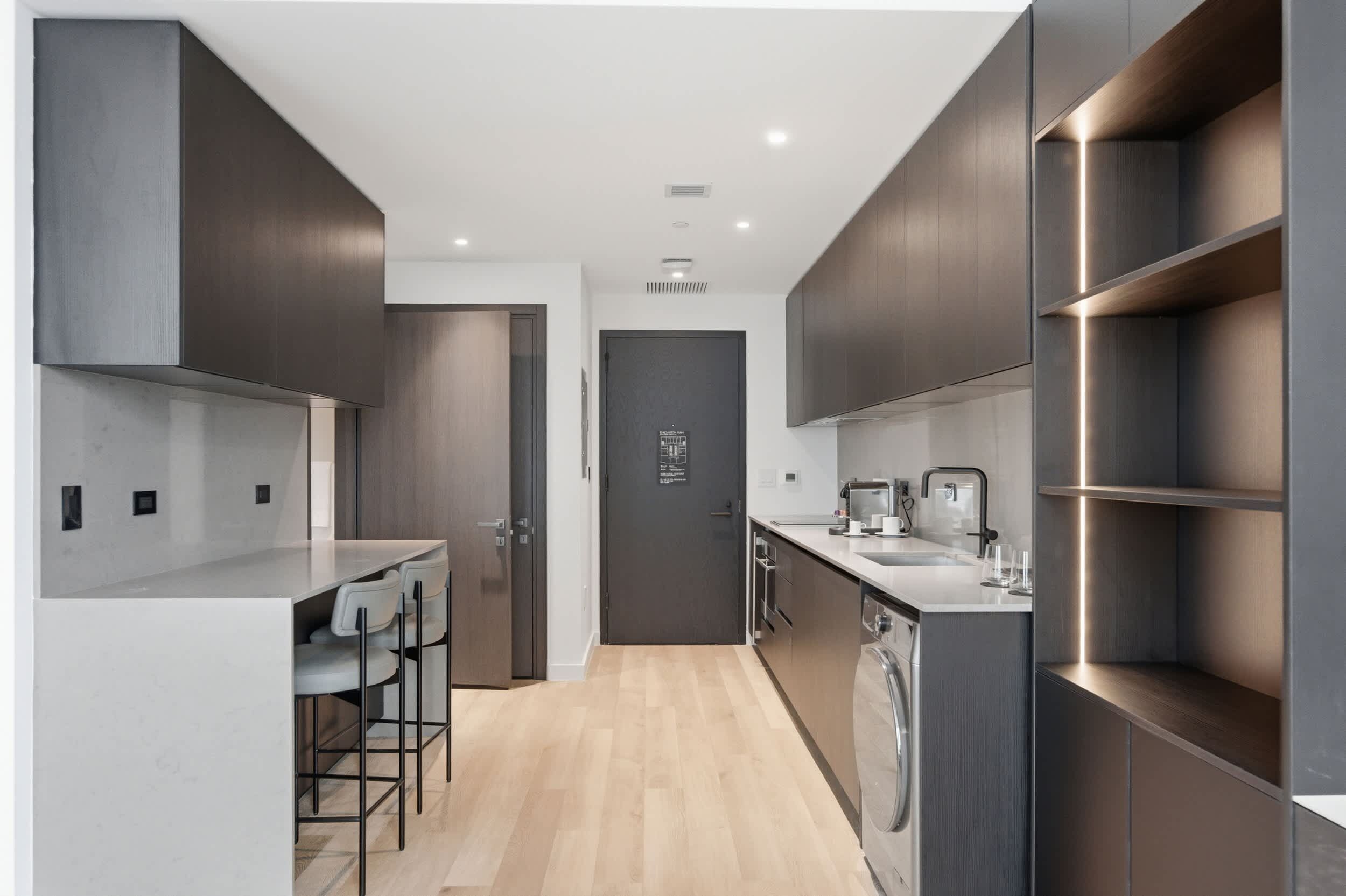 A modern kitchen with a central island, built-in appliances, and a dark wood finish.