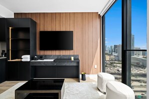 A modern living room with a large window, a flat-screen TV, a black sofa, and a coffee table. - Luxury E11EVEN Suite with Elite Pool & Views (Miami)