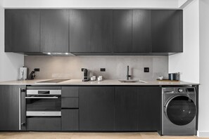 A modern kitchen with dark cabinetry, a built-in oven, a sink, and a washing machine. - E11EVEN Studio Suite w/ Rooftop Pool & City Views (Miami)