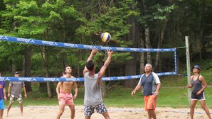 Eine Gruppe von Menschen spielt Beachvolleyball auf einem Sandplatz mit einem blauen Netz.