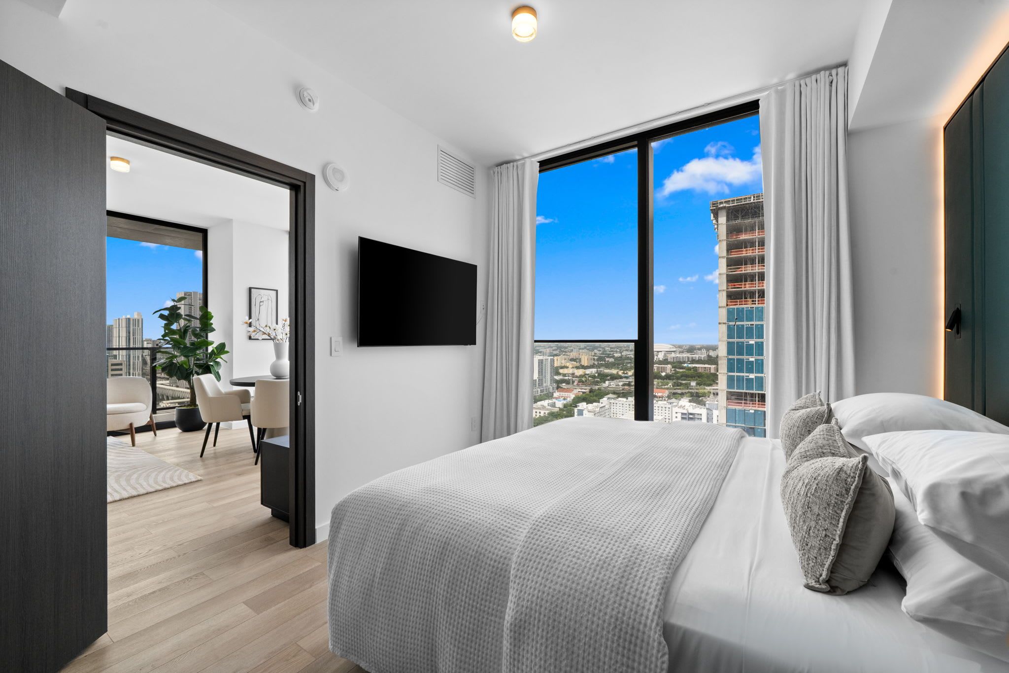 Ein modernes Hotelzimmer mit einem großen Bett, einem Flachbildfernseher, Blick auf die Stadt und einem Balkon mit Essbereich.