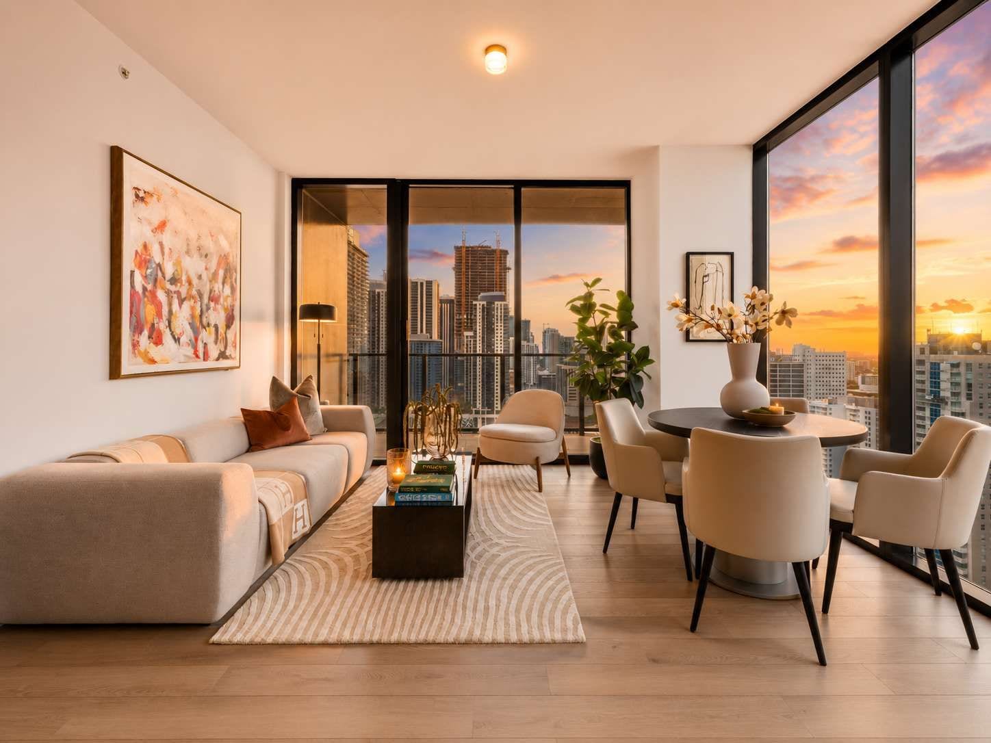 A modern living room with a sofa, chairs, a coffee table, and a view of a city skyline at sunset.