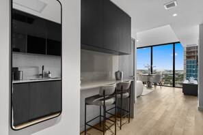 A modern kitchen with dark cabinets, a countertop, and a bar area with stools. - 26th Floor E11EVEN Retreat with Skyline & Bay Views (Miami)